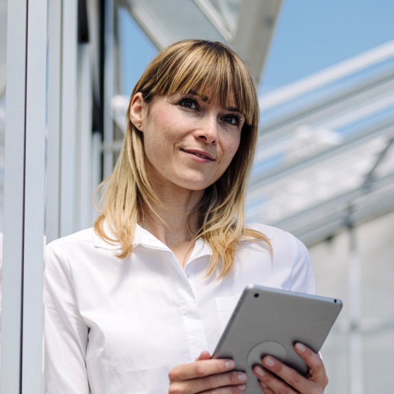 Femme d'affaires réfléchie tenant une tablette numérique tout en se tenant près du mur